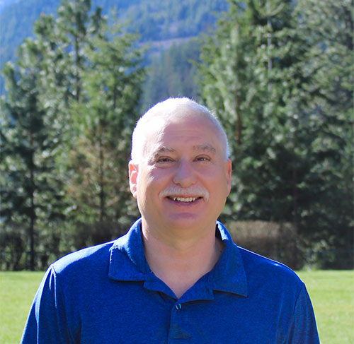 A smiling man with a mustache wearing a bright blue polo shirt.