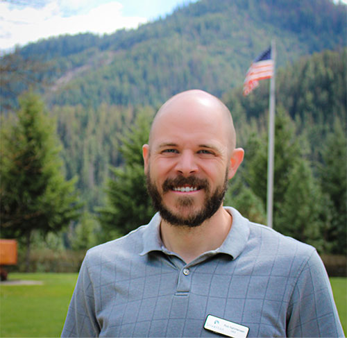 A smiling bald man with a beard wearing a light-grey polo shirt.
