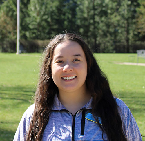 A smiling brunette woman wearing a light blue three-quarter zip jacket.